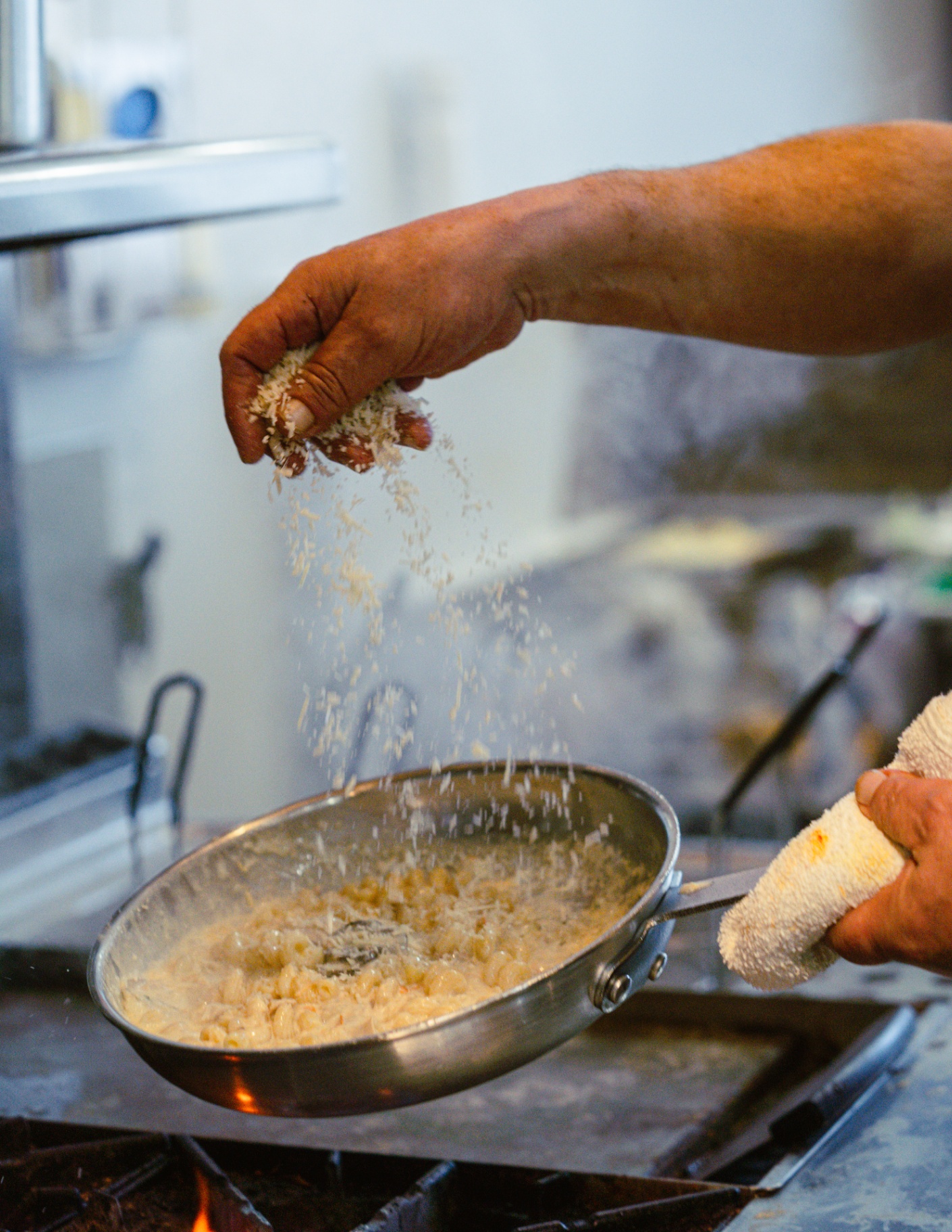 Chef finishing pasta with a shower of parmesan