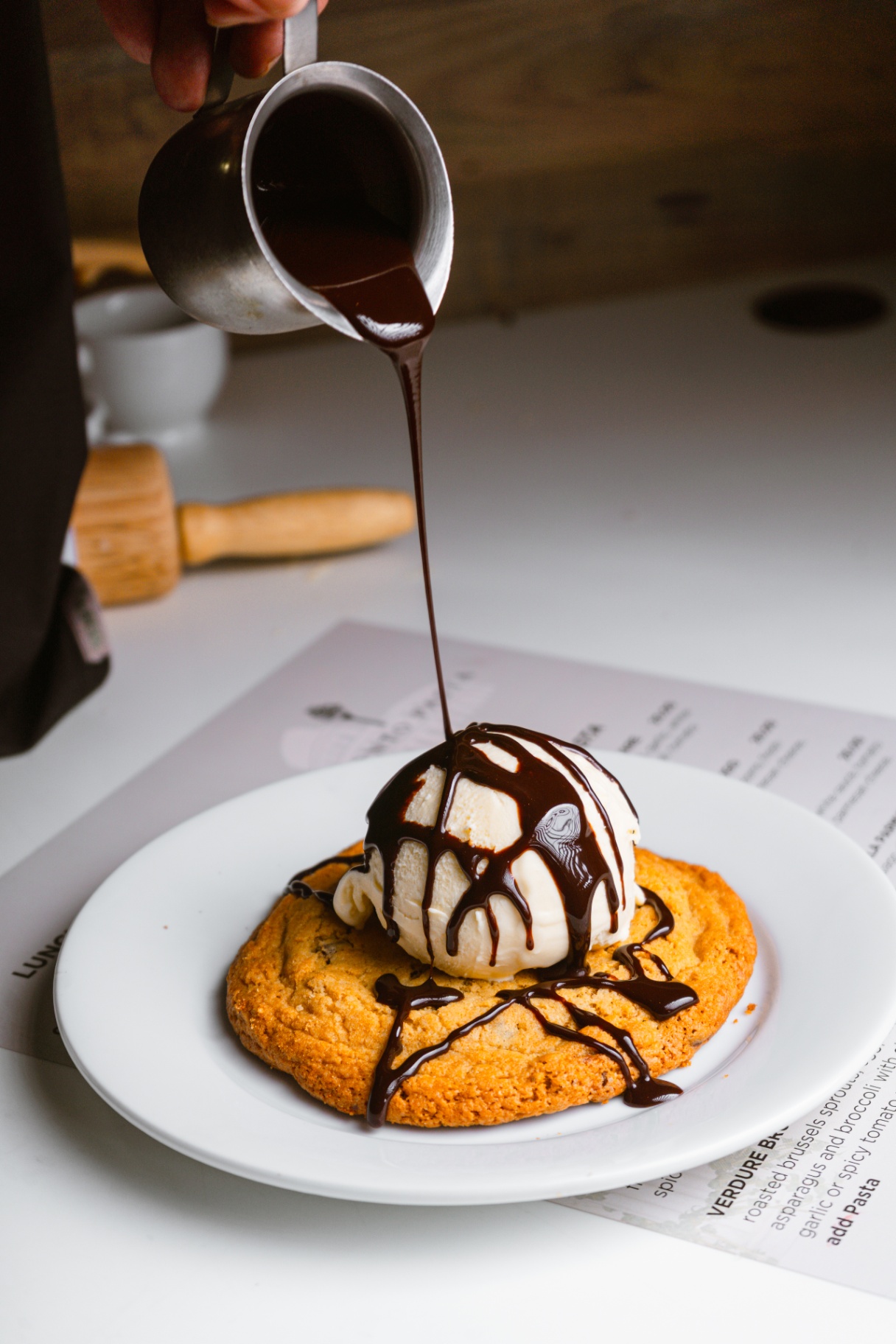 Warm cookie sundae with hot fudge being poured